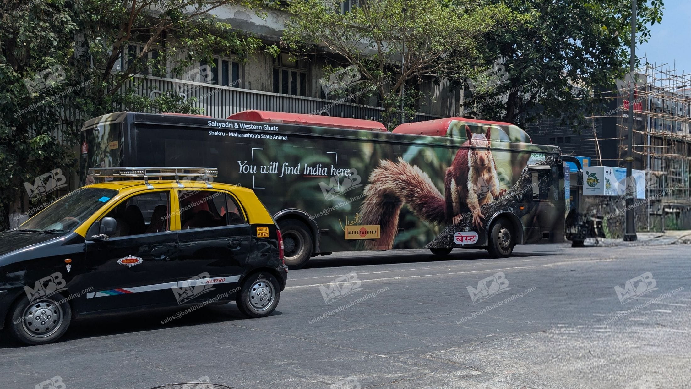 A BEST bus in Mumbai carrying a full-body Maharashtra Tourism wrap, passing a black-and-yellow taxi